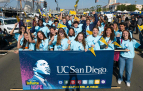 Slideshow: A large group of people wearing bright blue shirts stand behind a banner of Martin Luther King Jr