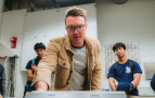 Slideshow: scientist in brown jacket talks to students in lab