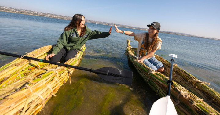 Slideshow: Two university students high five on tule boats.