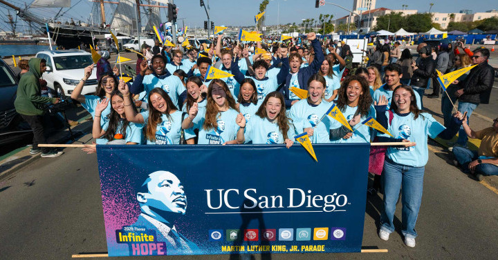 Slideshow: A large group of people wearing bright blue shirts stand behind a banner of Martin Luther King Jr