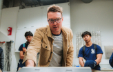 Slideshow: scientist in brown jacket talks to students in lab
