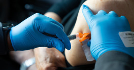 Close up photo of blue-gloved hands administering a vaccine in a person's arm. 