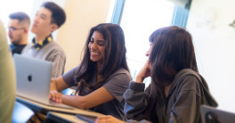 Photos focused on two female students sitting at a table with laptops open.