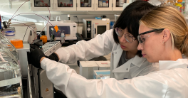Two female researchers in white lab coats analyzing samples with a mass spectrometer