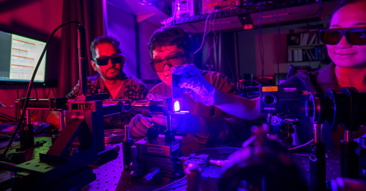 Three men working with a laser in a dimly lit lab.