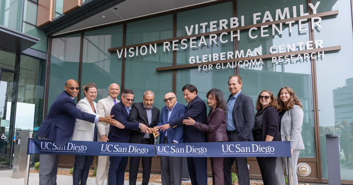 Group of people standing with two men holding a large pair of scissors, about to cut a large ribbon that says UC San Diego