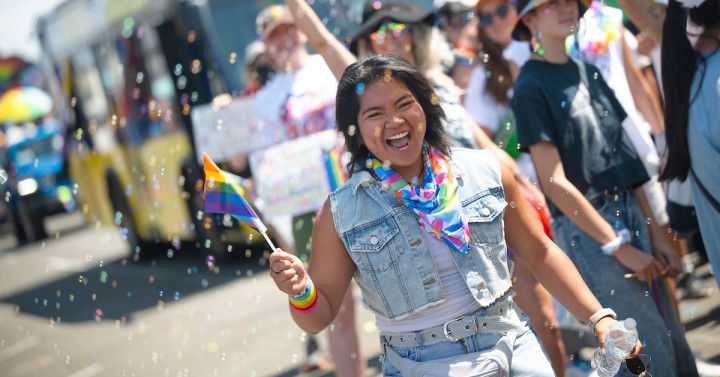 Young person holds pride flag with bubbles floating in air